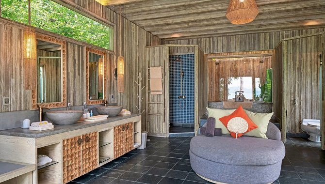 Rustikales Badezimmer mit zwei Waschbecken, großem Spiegel und gemütlicher Sitzecke.