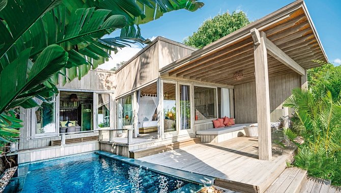 Villa mit Pool, großen Glasfronten und Holzveranda, umgeben von tropischen Pflanzen.