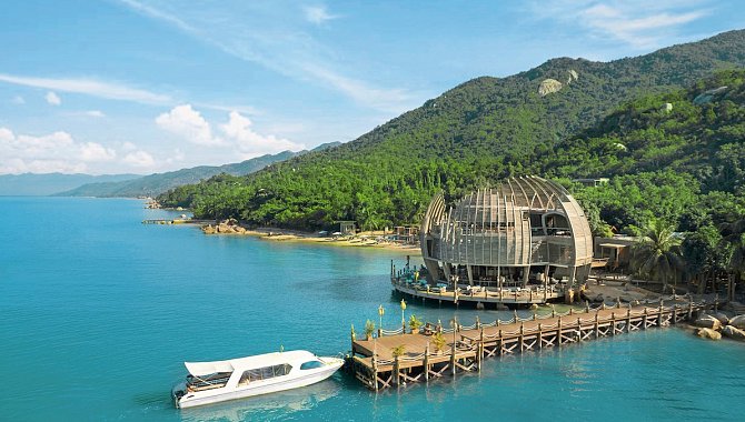 Bootssteg mit modernem Holzgebäude in ovaler Form über dem Wasser, dahinter grüne Hügel.