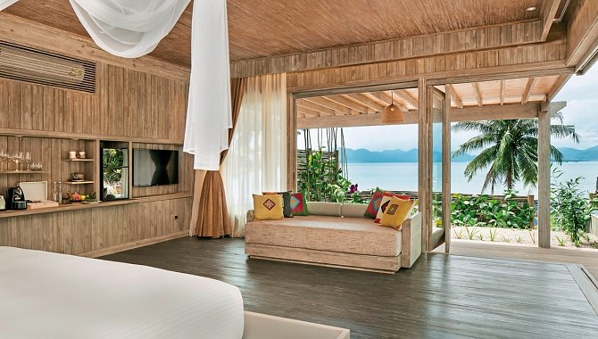 Helles Schlafzimmer mit Sofa und Blick auf das Meer durch große Glasfront.