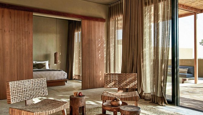 In diesem Zimmer sind Schlafbereich und das Wohnimmer durch eine großzügige hölzerne Schiebetür voneinander getrennt. Im Wohnzimmer stehen gewebte Sessel und Hölzerne runde beistelltische. Eine große Fensterfront mit leichten Vorhängen bietet Licht ohne zu viel Hitze hereinzulassen.