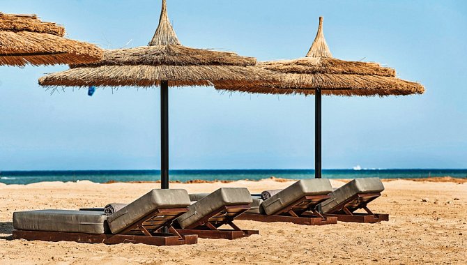 Am Strand finden sie gepolsterte Sonnenliegen und Sonnenschirme aus Stroh.