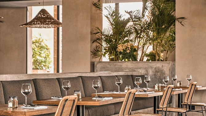 Eine gemütliche graue Sofareihe mit Holztischen davor und jeweils einem gewebten Stuhl.Der Tisch ist gedeckt mit Besteck und zwei Weingläsern.