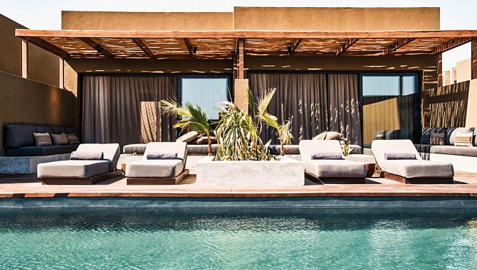 Ein Pool direkt vor einer Junior Suite. Zwei Junior Suites liegen direkt aneinander, die veranda ist mit einem Gewebten Sonnenschutz überdacht. In der Sonne vor dem pool stehen jeweils zwei gepolsterte Poolliegen.