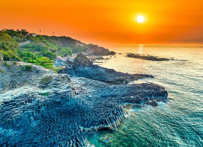Basaltfelsen von Ganh Da Dia in Phu Yen bei Sonnenuntergang, mit leuchtendem Himmel und Meer im Hintergrund.