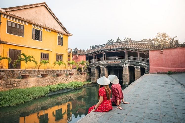Zwei Frauen in traditionellen vietnamesischen Kleidern vor der historischen Japanischen Brücke in Hoi An.
