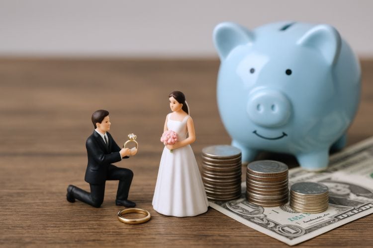 Miniatur-Brautpaar mit Geldstapel und Sparschwein als Symbol für Hochzeitskosten und Budgetplanung