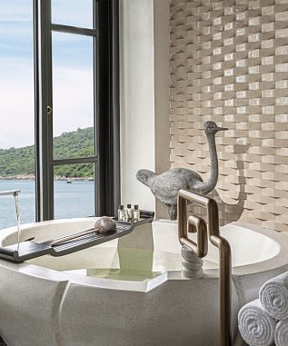 Freistehende Badewanne mit Aussicht auf das Meer, daneben dekorative Statue