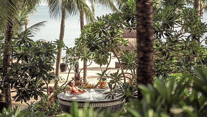 Frau im Whirlpool, umgeben von tropischen Pflanzen und Blick aufs Meer