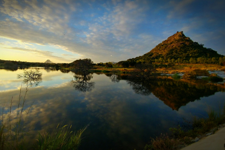 Spiegelglatter See im Gorongosa-Nationalpark mit bewaldeten Hügeln im Abendlicht.