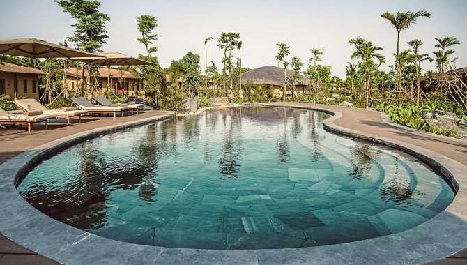 Runder Außenpool umgeben von Palmen und Sonnenliegen