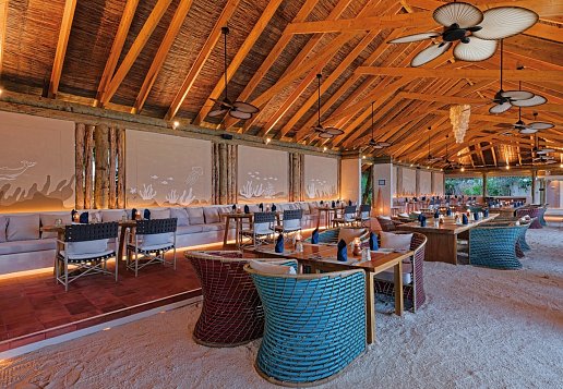 Hotelrestaurant, überdacht am Strand mit gemütlichen Korbsesseln und vierer Tischen