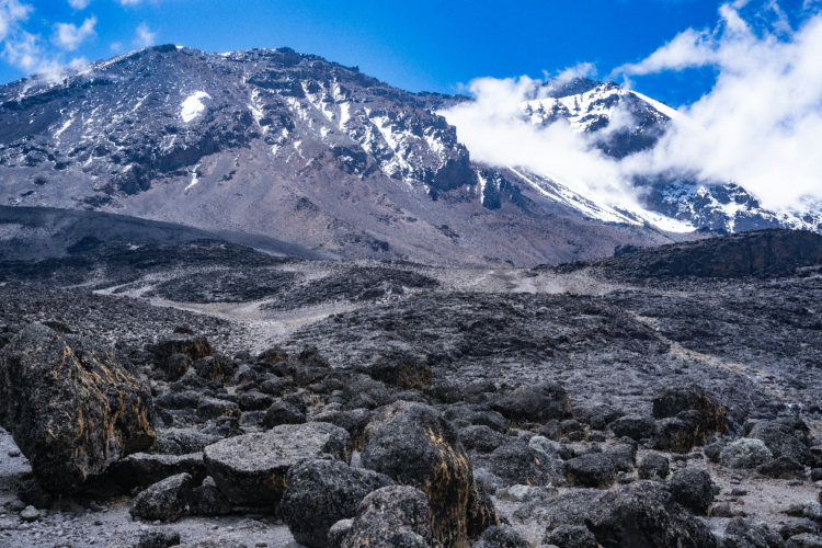 Felsenlandschaft am Kilimandscharo mit schneebedeckten Gipfeln und Wolken im Hintergrund.