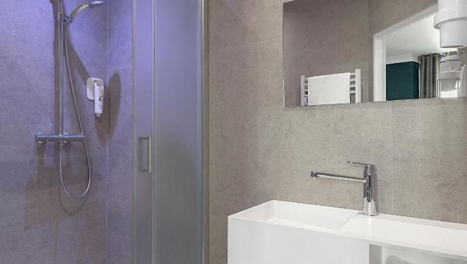 Modernes Badezimmer mit ebenerdiger Dusche, Waschbecken und großem Wandspiegel im Hotel The Originals Boutique