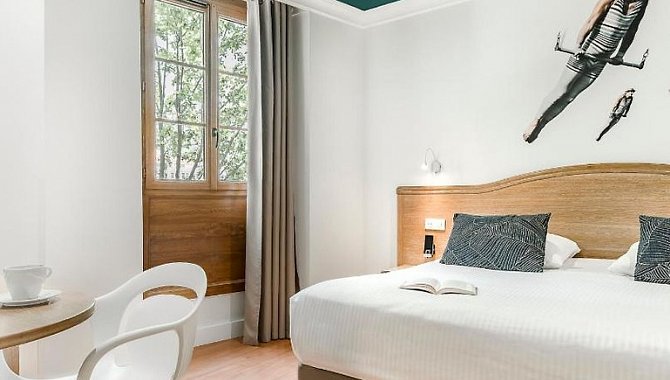 Helles Hotelzimmer mit Doppelbett, Schreibtisch, Sitzgelegenheit und Fenster im Hotel The Originals Boutique