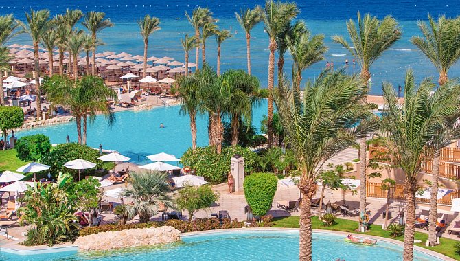 Poolanlage des Hotels aus der Vogelperspektive. Man sieht die Palmen und das Meer. Dazwischen die vielen Sonnenschirme und Poolliegen.