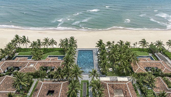 Luftaufnahme mit Pool in der Mitte, flankiert von Palmen und Strand dahinter.
