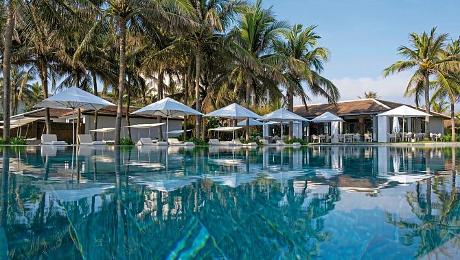 Großer Pool mit weißen Sonnenschirmen und Palmen ringsum.