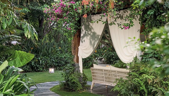 Überdachte Gartensitzecke mit weißen Vorhängen und blühenden Pflanzen