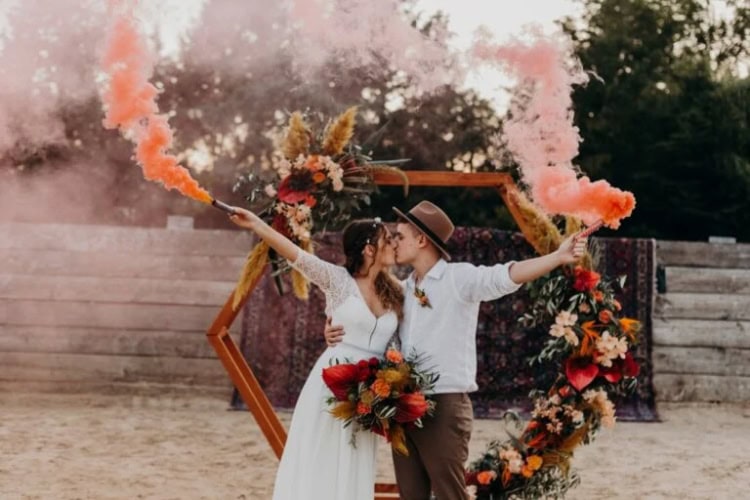 Paar steht mit Fakeln vor einem Hochzeitsbogen und küsst sich